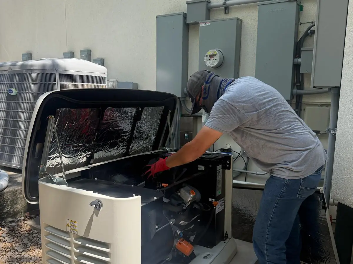 A ProTeks technician servicing the engine of a standby generator, its lid raised and the oil filter visible