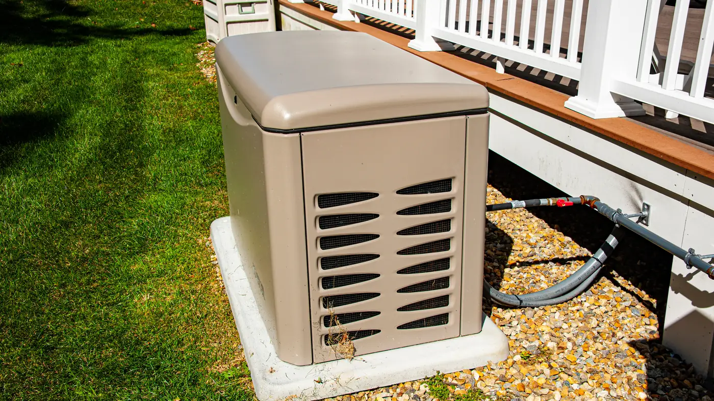 A residential standby generator on a concrete pad beside a house, gas line connected