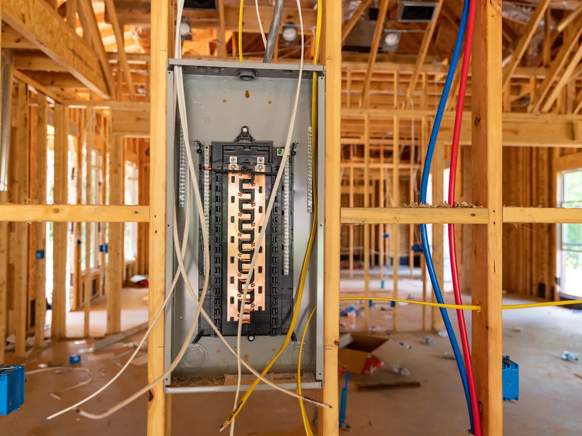An open breaker panel and its wiring, mounted between bare studs in a house under construction