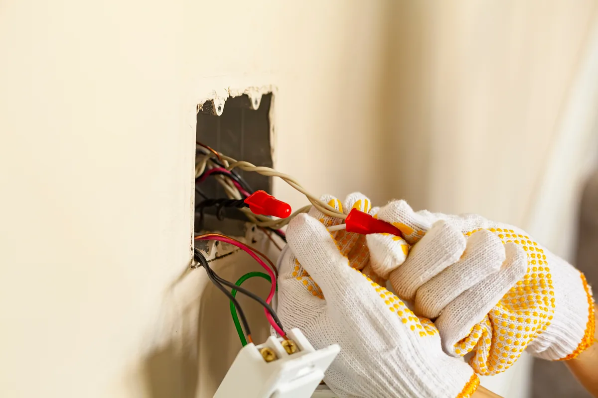 Gloved hands connecting wires at an electrical box cut into a wall