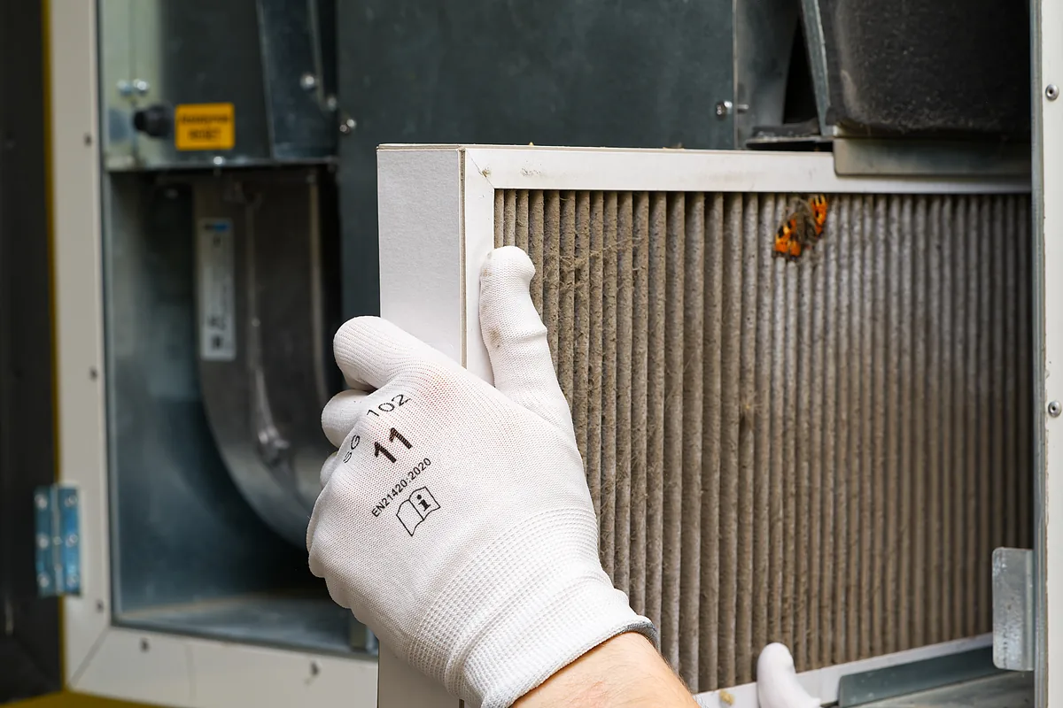 A gloved hand pulling a clogged, dust-covered filter out of an air handler